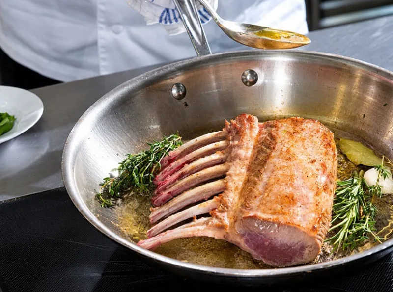 Lammrack in der Pfanne wird mit Kräutern und Butter arrosiert